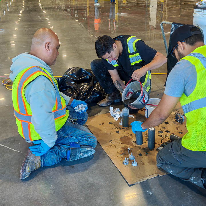 Epoxy flooring contractors working on a commercial job site, pouring and spreading self-leveling floor coatings.