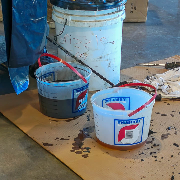Several blue mixing pails and containers filled with colorful resin coatings on a workshop floor during an installation.
