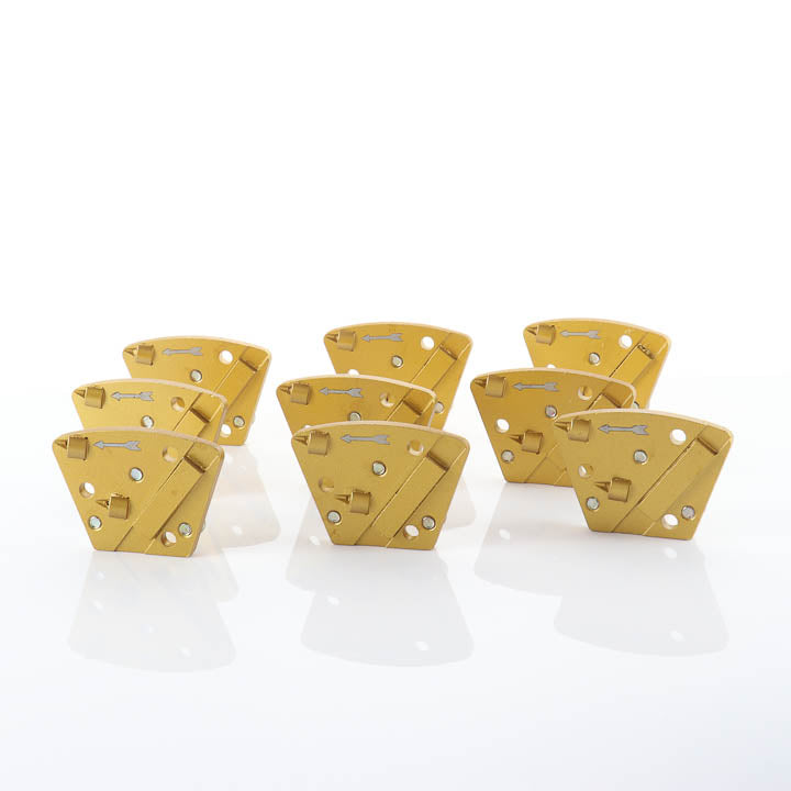 Gold-colored trapezoid PCD diamond grinding shoe for concrete floor grinders, featuring two pointed PCD segments, one diamond bar, a left-facing directional arrow, and three countersunk mounting holes on a white background Full set of 9