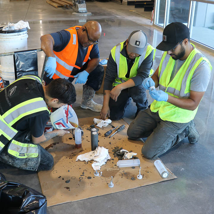 Epoxy flooring contractors working on a commercial job site, pouring and spreading self-leveling floor coatings.